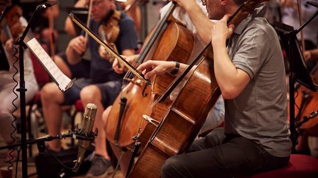 Cellists playing in a studio recording session with microphones in front of the instruments
